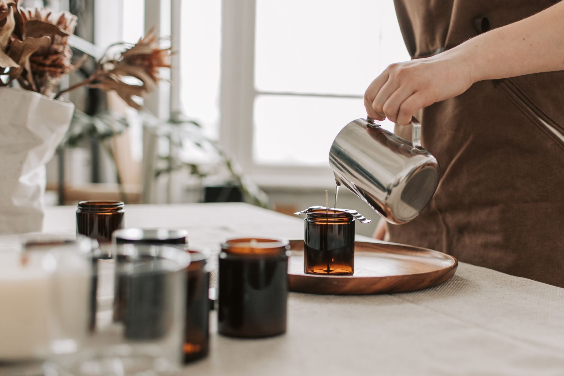 Close-up of a woman pouring wax into jars for handmade candle making.